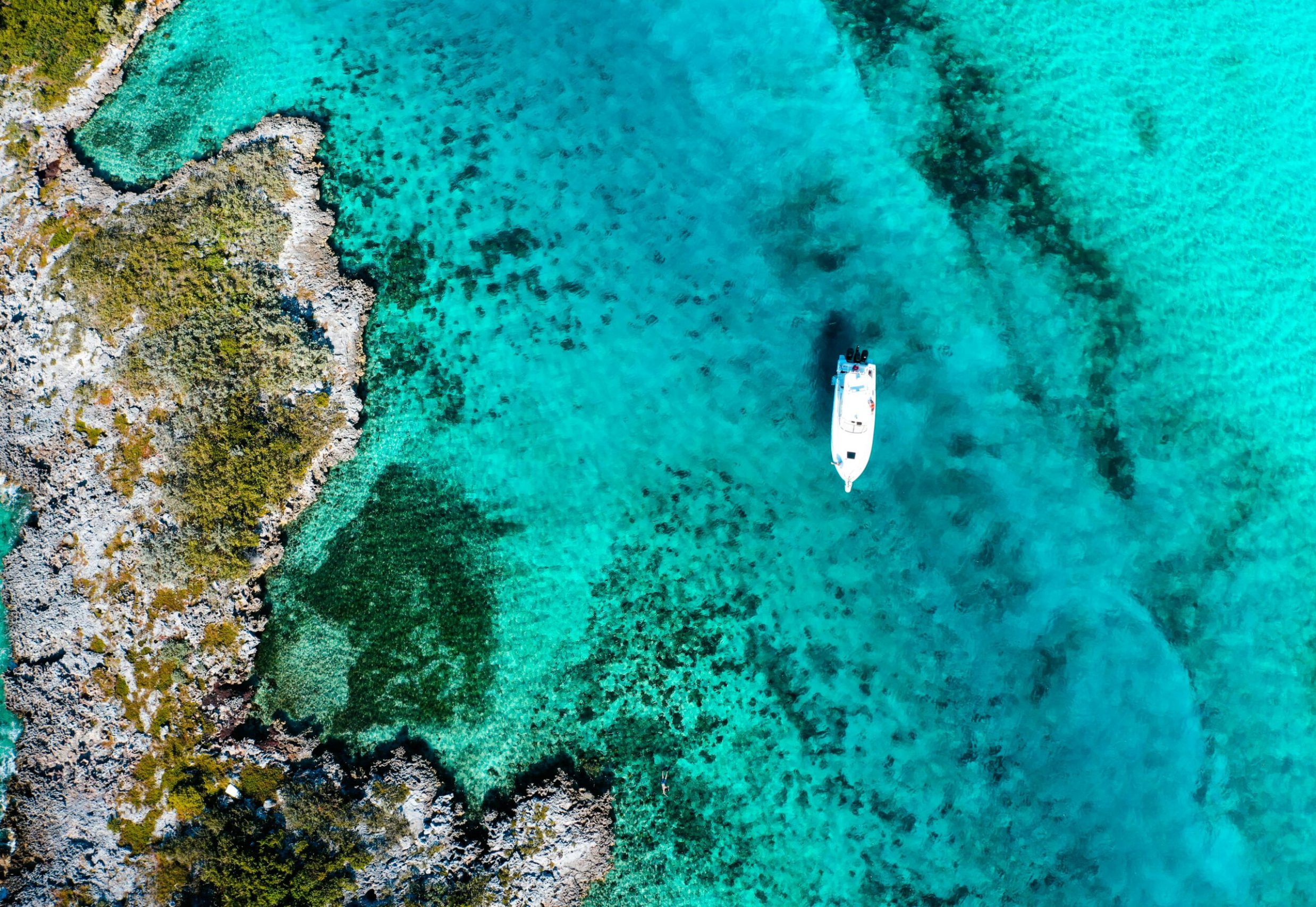 Aerial shot of a boat floating in the turquoise waters of the Bahamas, showcasing vibrant coral reefs.